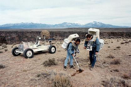Training zu Apollo 15, Foto-Nr. S71-23772,
                        EVa-Exkursion in mondähnlicher Landschaft in
                        Taos am Rand des Rio Grande (New Mexico): Irvin
                        nimmt Bodenproben mit einer Schaufel, Scott hält
                        einen Beutel für die Bodenprobe,
                        Trainingsmondauto "Grover" im
                        Hintergrund, 11.-12.3.1971, Katalogdatum
                        3.11.1971.