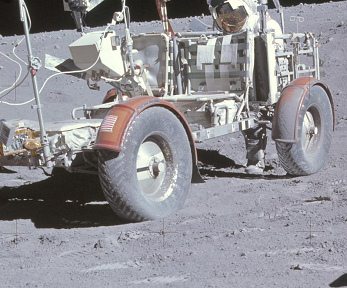 Apollo 16 Foto-Nr. AS16-107-17537:
                            Astronaut Duke hinter dem
                            "Mondauto" ohne Reifenspuren
                            zwischen Vorder- und Hinterreifen,
                            Nahaufnahme.