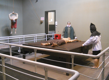 "Christian" torture with a
                            rack (stretching bank, extension bed) and in
                            the background can be seen torture by
                            hanging